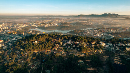 An aerial view of Da Lat city nestled among green hills, with a lake in the foreground.