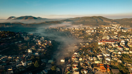 An aerial view of Da Lat city nestled among green hills, with a lake in the foreground.