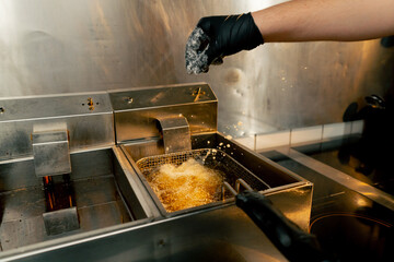 professional kitchen with double fryer into which the chef throws chicken wings in flour