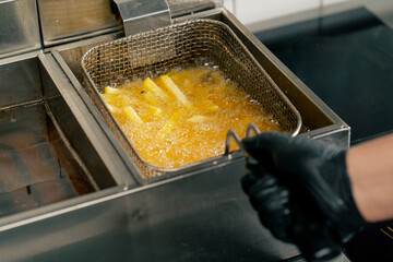 close-up in professional kitchen frying French fries in oil in a deep fryer