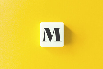 Capital Letter M. Text on Block Letter Tiles against Yellow Background.