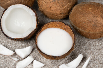 Coconut milk in coconut shell and half coconut, chopped flesh on grey background