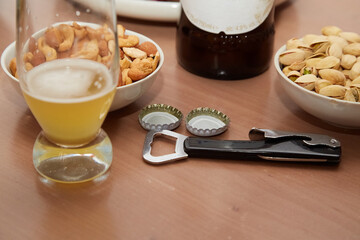 Bottle opener; beer glass with unfinished beer; bowls of nuts on the table close-up; beer snacks;...