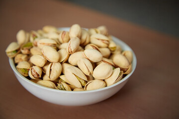 A plate of pistachios stands on a wooden table, pistachios in a plate, a plate of salted pistachios