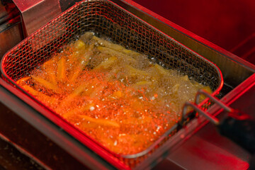 close-up in professional kitchen frying French fries in oil in a deep fryer red light