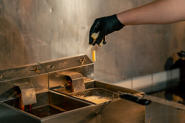 close-up in a professional kitchen, the chef throws French fries into the fryer