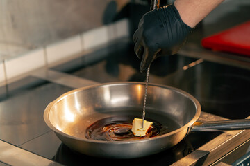 close-up in a professional kitchen the chef uses a knife to distribute oil in a frying pan