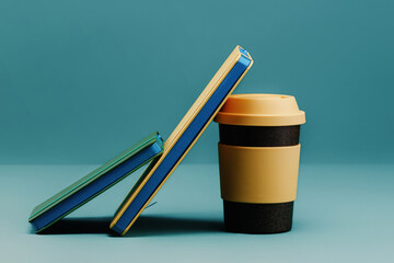Notebooks lean on a reusable cup with rubber lid on a blue background. The concept of an...