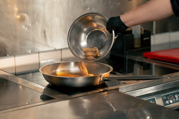 close-up in professional kitchen the chef throws chicken wings into a frying pan with sauce