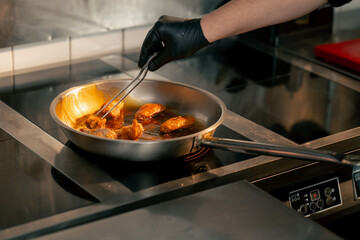 close-up in a professional kitchen chicken wings are fried in a frying pan with sauce the chef...