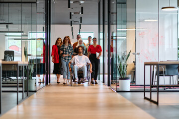 A diverse group of young business people walking a corridor in the glass-enclosed office of a modern startup, including a person in a wheelchair and a woman wearing a hijab