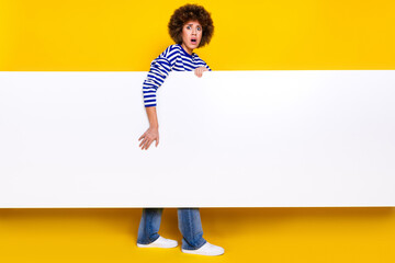 Full size photo of frightened girl wear striped pullover hold banner empty space astonished staring...