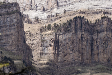 Rocky cliffs with distinct layers and erosion patterns, surrounded by sparse vegetation under a clear sky, showcase nature’s artwork