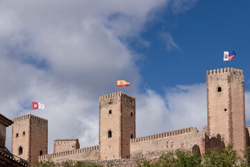 A serene, ancient stone castle with distinct flags atop towers under a partly cloudy sky, devoid of...