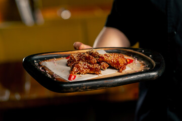 close up hand in a restaurant a chef in a black jacket stands with a prepared Chicken wings