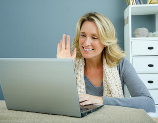 Portrait of 40 year old blonde happy smiling woman in video conference computer screen at home