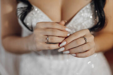 A woman is wearing a white dress and holding her hands up to show off her wedding ring. The ring is...