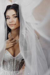 A woman is wearing a white wedding dress and is posing for a picture. She is wearing a necklace and has her arms around her neck. The image has a romantic and elegant mood