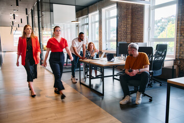 A diverse group of business professionals collaborates in a modern startup coworking center, utilizing a mix of paper-based and technological tools such as mobile phones and computers to collectively