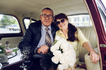 elderly man and a woman on a walk in the city in a vintage car with a bouquet of flowers