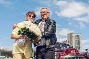 elderly man and a woman on a walk in the city in a vintage car with a bouquet of flowers