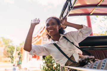 black tourist girl head out waving holding tuk tuk bar. young african american tourist using bar...
