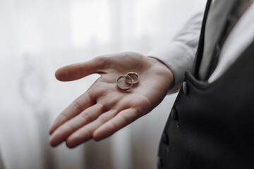 A man is holding two gold wedding rings in his hand. The rings are placed on top of each other, and the man is wearing a suit. Concept of love and commitment
