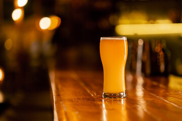 close up in the bar there is glass of beer on a wooden bar counter in the rays of the sun