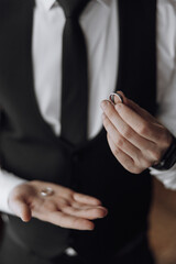 Obraz premium A man in a suit holding a ring in his hand. The man is wearing a black tie and a black vest