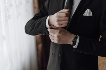 A man in a suit is getting ready to tie his tie. He is wearing a black suit and a white shirt