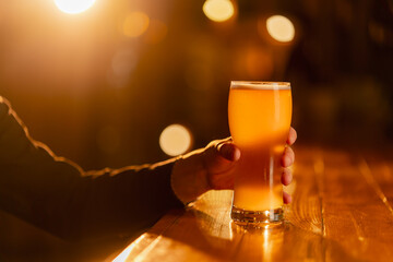 close-up on a wooden bar table guy holds a glass of light beer warm lighting light