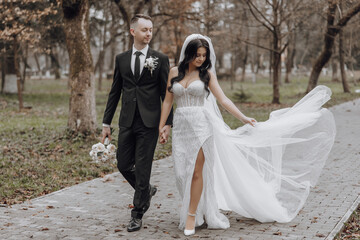 A bride and groom are walking down a path in a park. The bride is wearing a white dress and the groom is wearing a suit. They are holding hands and the bride is carrying a bouquet