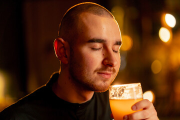 close-up on a wooden bar table guy sniffs a glass of light beer warm lighting light