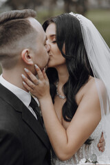 A bride and groom kiss in a wedding photo. The bride is wearing a veil and the groom is wearing a tie