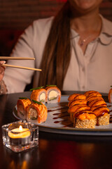 Young woman eats and enjoys fresh sushi in a luxurious restaurant. Girl holds chopsticks in her hands and eats a delicious set of sushi. Traditional Japanese dish. Concept of food. Vertical photo
