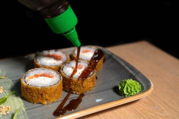 Close-up chef pours teriyaki sauce over hot Banzai sushi with salmon, rice, cream cheese, sesame...