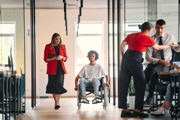 A business leader with her colleague, an African-American businessman who is a disabled person, pass by their colleagues who work in modern offices