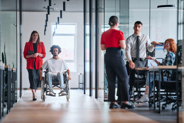 Obraz premium A business leader with her colleague, an African-American businessman who is a disabled person, pass by their colleagues who work in modern offices