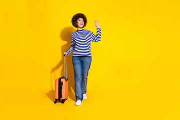 Full size photo of friendly girl wear striped pullover hold baggage waving palm look empty space...