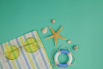 on a delicate green-blue background, shells of different shapes and sizes, a beach towel, yellow...