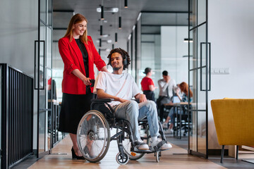 A business leader with her colleague, an African-American businessman who is a disabled person, pass by their colleagues who work in modern offices