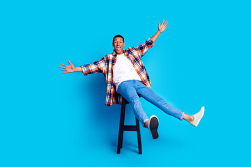 Full size photo of nice young man sit stool raise arms wear shirt isolated on blue color background