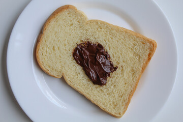 One slice of white bread and one scoop of chocolate spread, on white plate, isolated on white background, flat lay or top view