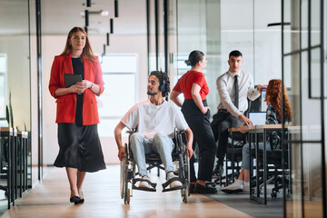 A business leader with her colleague, an African-American businessman who is a disabled person, pass by their colleagues who work in modern offices