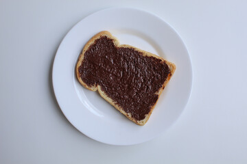 One slice of white bread, covered by chocolate spread, on white plate, isolated on white background. Prepare chocolate sandwich. Flat lay or top view