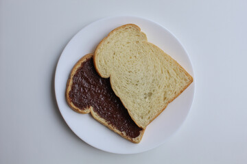 Two slices of white bread with chocolate spread or chocolate jam. Chocolate sandwich. On white plate, isolated on white background, flat lay or top view