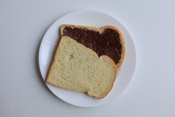 Two slices of white bread with chocolate spread or chocolate jam. Chocolate sandwich. On white plate, isolated on white background, flat lay or top view