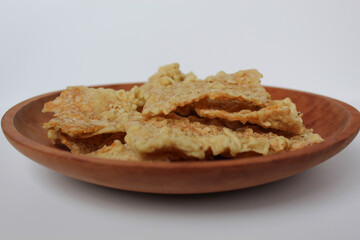 Keripik tempe or tempeh crackers, square shape. Thin slices tempeh, fried with flour dough. On wooden plate, isolated in white background