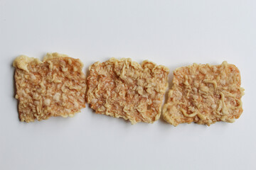 Three pieces of keripik tempe or tempeh crackers, square shape. Thin slices tempeh, fried with flour dough. Isolated in white background, flat lay or top view