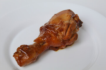 Ayam Kecap, or chicken cooked with sweet soy sauce. One chicken drumstick on white plate, isolated on white background